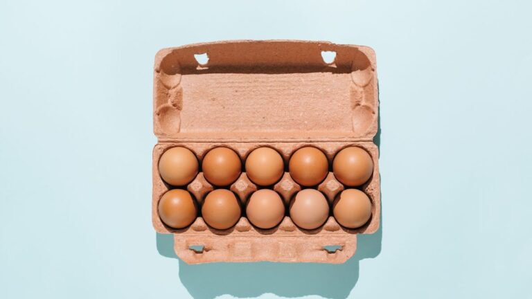 Holiday Cooking Prep: Here’s Exactly How Long Eggs Last in Your Fridge A carton of brown eggs against a blue background.