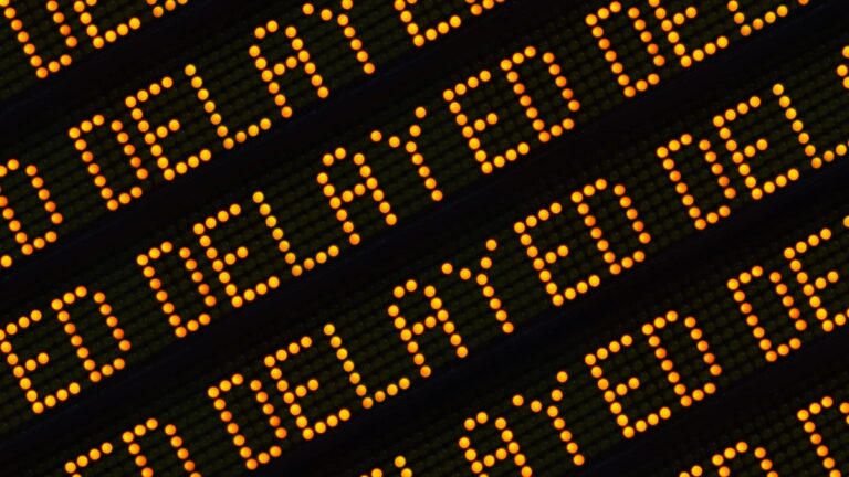 an LED screen displaying diagonally tiletd rows and rows of the word "delayed" in all capital letters