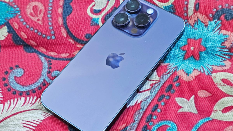 a black Apple iPhone sits face down on a light wood-grained table