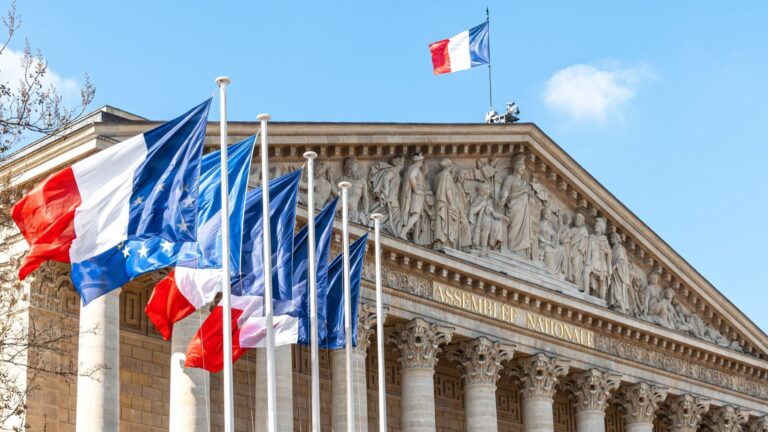 View on National Assembly building in Paris, France, with French and European flags flying.