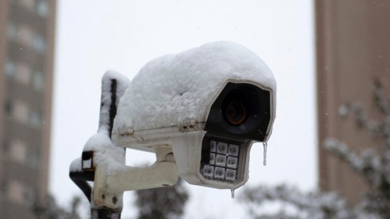 An old security camera outdoors is covered in snow.