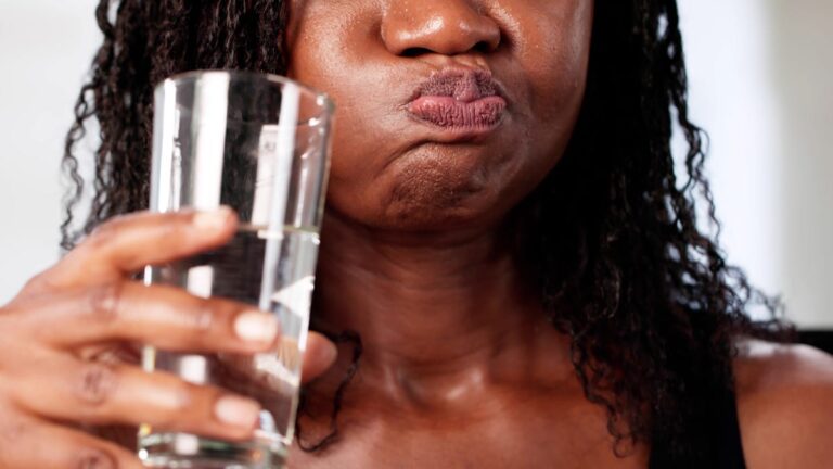 A person holding a glass is swishing their mouth with water.