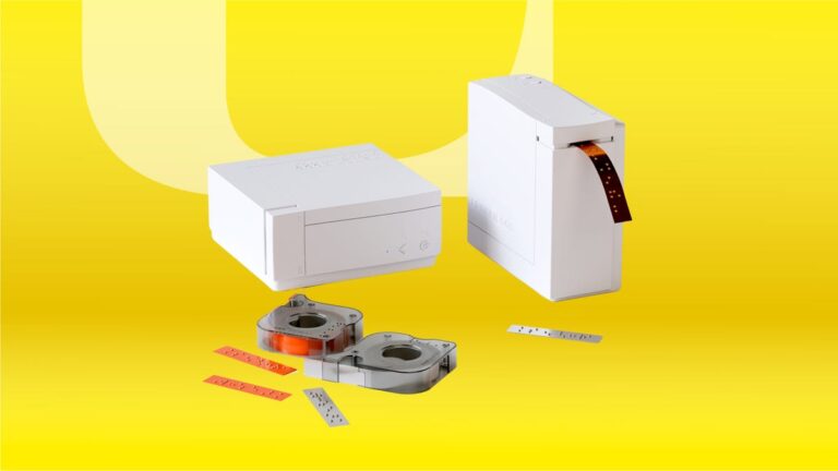 This Braille Label Printer Helps Blind Friends and Family Grab the Right Pill Bottle A rectangular printer with labels sticking out.