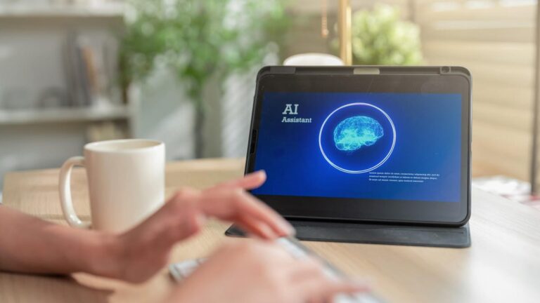 5 Ways to Get Advanced AI Monitoring at Your Home for Free Hands type on a keyboard next to a mug and a tablet screen showing an AI assistant.