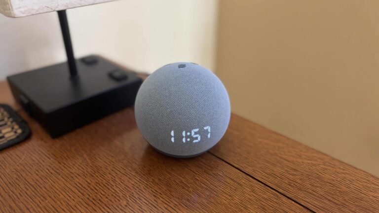 An Echo Dot with LED clock on a wooden table by a lamp